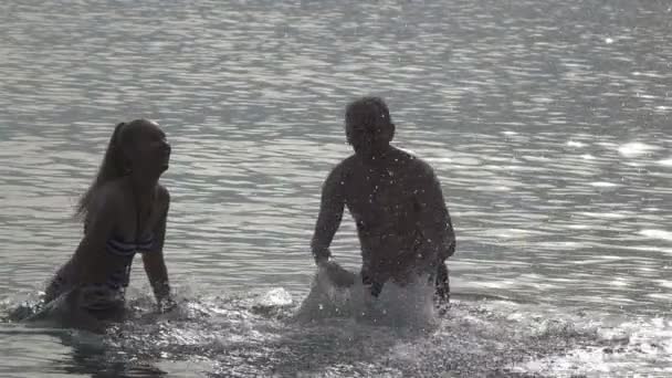 La silhouette des jeunes de l'homme et de la femme qui se tiennent dans la mer et éclabousse les mains de l'eau, au ralenti — Video