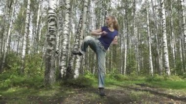 Dövüş sanatları bir orman glade, ağır çekim üzerinde bir t-shirt ve jeans içinde uzun svetly saçlı genç ince kadın yok
