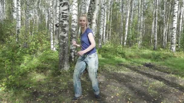 De jonge slanke vrouw met lang svetly haren in een t-shirt en jeans doet vechten martial arts op een bos glade, slow-motion — Stockvideo