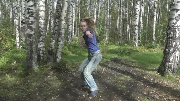 A mulher esbelta jovem com o cabelo svetly longo em uma camiseta e calça faz a luta contra artes marciais em uma clareira florestal, câmera lenta — Vídeo de Stock