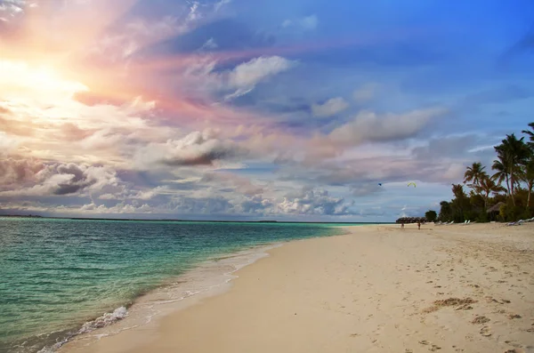 Maldivler. Güneş bulutların üzerinden ışık palmiye ağaçları ile plaj