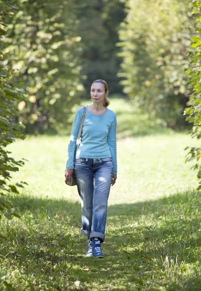 A fiatal nő a kék kabát sétál a parkban nyári. — Stock Fotó