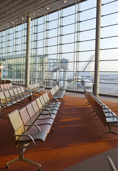 Poltronas vazias na sala de espera do aeroporto e avião atrás da janela — Fotografia de Stock