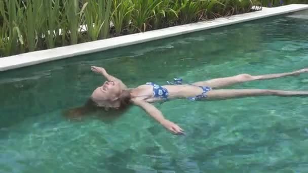 Η νεαρή λεπτή γυναίκα με μακριά μαλλιά στο Bikin που κολυμπά στην πισίνα κάτω από φοίνικες στο τροπικό θέρετρο — Αρχείο Βίντεο