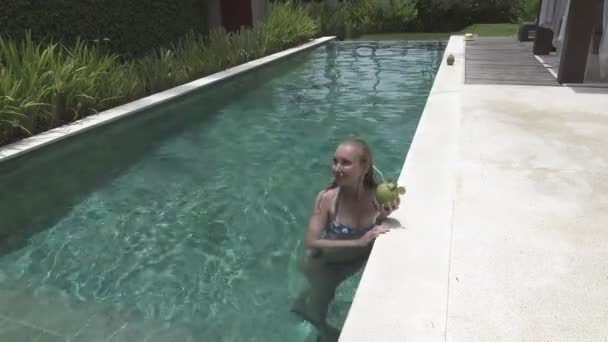 La giovane donna snella con i capelli lunghi ha un riposo in piscina e beve cocktail da cocco nella località tropicale — Video Stock