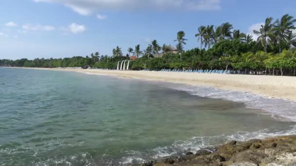 Panorama z písečné pláže lehátka a slunečníky v tropickém letovisku. Bali. Indonésie — Stock video