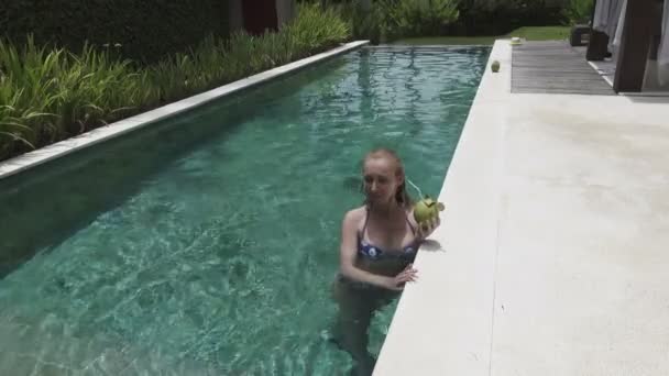 Η νεαρή λεπτή γυναίκα με μακριά μαλλιά έχει ένα υπόλοιπο στην πισίνα και κοκτέιλ ποτών από καρύδα στο τροπικό θέρετρο — Αρχείο Βίντεο