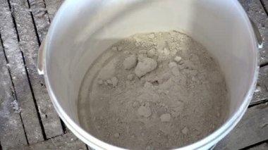 İnşaat ustası, kuru inşaat karışımını elle karıştırıcı ile yoğurmak için kaba döker. 4K Uhd 'da ısıtılır.