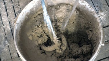 Su akıntısı, inşaat mikseri ve alçıyla bir kovaya dökülüyor.