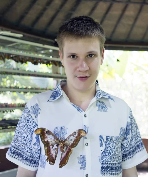 在蝴蝶公园里的年轻人 衬衫上戴着一只大的热带蝴蝶 — 图库照片