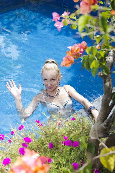 游泳池里穿着敞开式游泳衣的美丽瘦弱的女人在镜头前挥手 穿过热带植物射击 — 图库照片