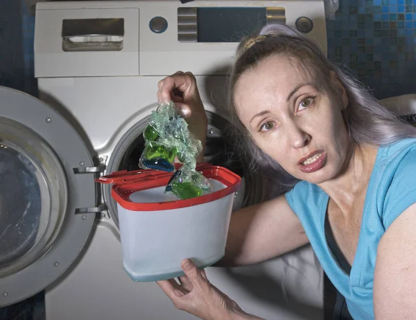 洗濯機の横にある浴室の女性は欠陥のある洗浄ジェルを包装から一塊に詰め込み — ストック写真