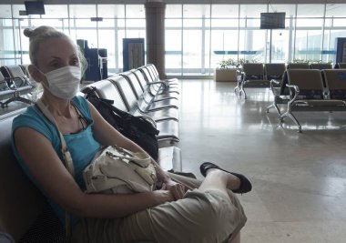 Tıbbi koruyucu maskeli kadın, Coronavirüs salgını sırasında boş bir havaalanı salonunda oturuyor..