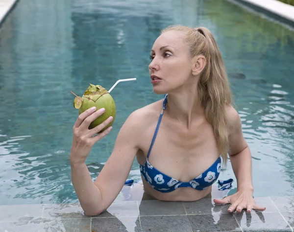 一位年轻貌美的女人 一头长发 身穿泳衣 在游泳池里喝着椰子鸡尾酒 — 图库照片