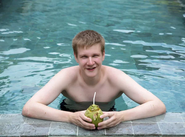happy young man in pool with coconut cocktail