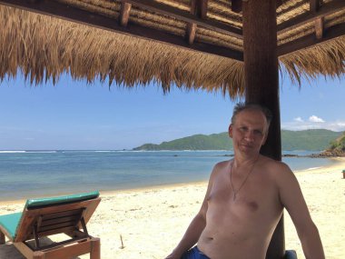 Boş sahil ve denizin arka planında mutlu bir adam var. Lombok, Endonezya.
