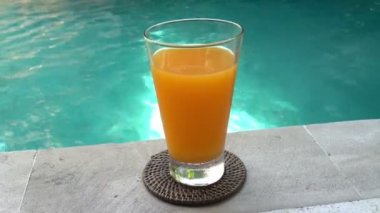 Tropik bir tatil köyünde, yüzme havuzunun kenarında suyun ortasında bir bardak meyve suyu.