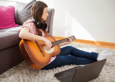 Güzel ve genç birbayan öğrenmek klasik gitar Internet üzerinden laptop yanında evde oynamak.