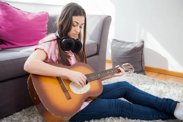 stock image Young woman playing on acoustic guitar, sitting on floor in casual clothes at home