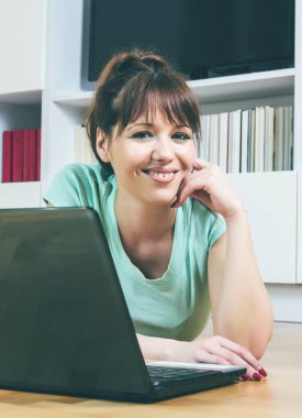 Evde dizüstü bilgisayar kullanan mutlu, genç bir kadın..