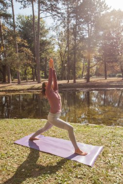 Güzel bir sonbahar sabahında gölün yanındaki parkta yoga egzersizi yapan genç bir kadın..