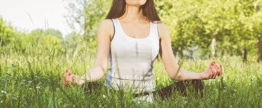 Güneşli bir günde parkta kadın meditasyon yapıyor ve yoga yapıyor.