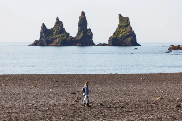 Женщина, прогуливающаяся по пляжу, глядя на выдающийся морской стек — стоковое фото