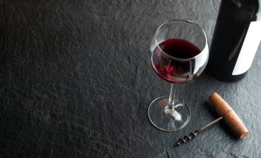 Şarap şişesi, tirbuşon ve arka planda şarap kadehi.