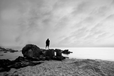 Kumlu sahilde kaya üzerinde duran genç adamın silueti