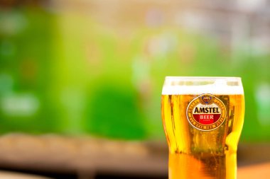 SOFIA, BULGARIA - MAY 08, 2017: Close-up Amstel glass full of beer -background of tv playing football game.Amstel Premium Pilsener is an internationally known brand of beer produced by Heineken Intern clipart