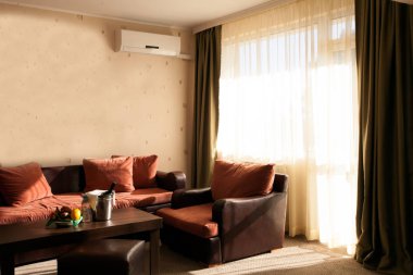 Oteldeki parlak ve rahat modern oturma odası, geniş pencere ve geniş pencere pervazı yumuşak koltuklar ve minderlerle okumak için.