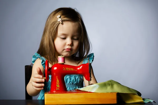 Little girl is playing with sewing machine — Stock Photo, Image