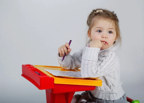 Улыбающаяся маленькая девочка за столом рисует — стоковое фото