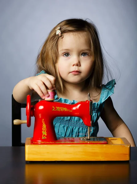 Menina está brincando com a máquina de costura — Fotografia de Stock