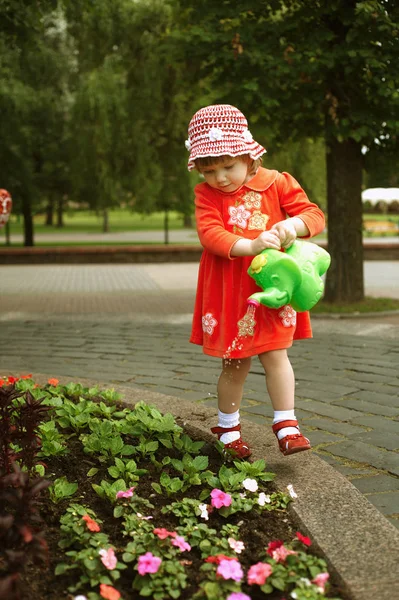 Söt flicka vattna blommorna i trädgården — Stockfoto