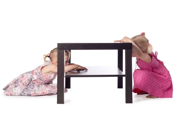 Two little girls hiding behind table — Stock Photo, Image