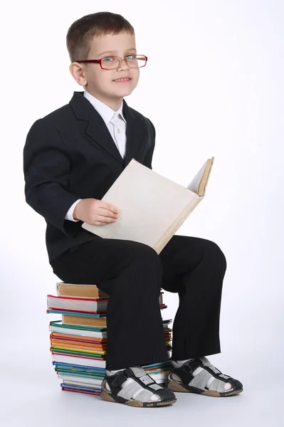 Boy makes homework sitting on stack of books — Stock Photo, Image