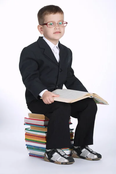 Boy makes homework sitting on stack of books — Stock Photo, Image