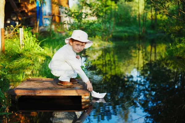 Menina brinca com barco de papel no rio — Fotografia de Stock