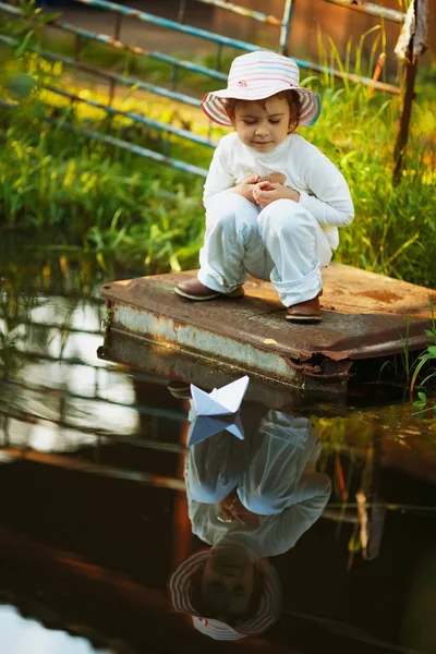 Meisje speelt met papier boot in de rivier — Stockfoto