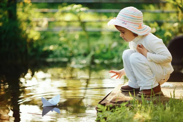 Chica juega con papel barco en el río — Foto de Stock