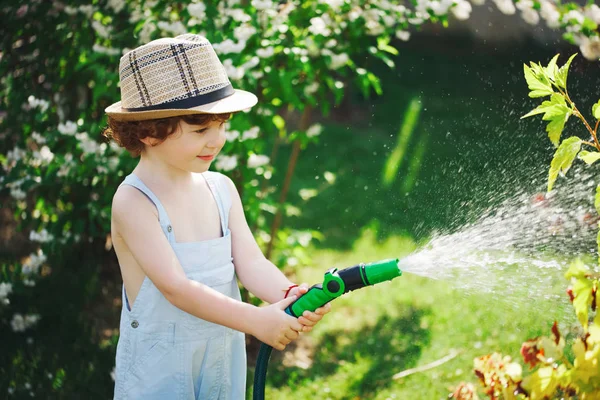 Kleiner Junge wässert den Garten mit Schlauch — Stockfoto