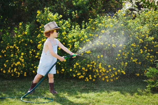Маленький хлопчик поливає сад шлангом — стокове фото