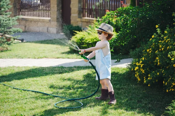 Маленький хлопчик поливає сад шлангом — стокове фото