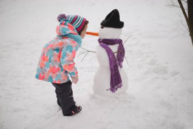 Kız kardan adam kış parkta yapar.
