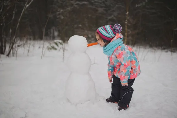 Dziewczyna sprawia, że snowman w winter park — Zdjęcie stockowe