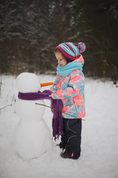 Girl makes snowman in winter park — Stock Photo, Image