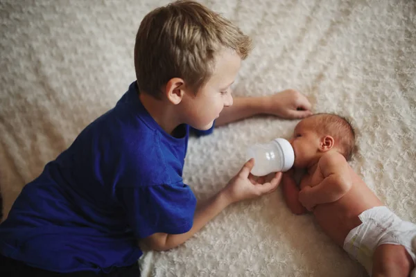 Garçon nourrissant bébé nouveau-né avec une bouteille de lait — Photo