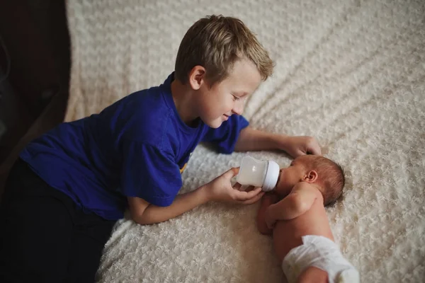 Хлопчик годує новонароджену дитину пляшкою молока — стокове фото