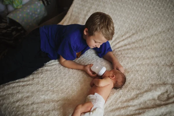 Niño alimentando al bebé recién nacido con biberón de leche —  Fotos de Stock